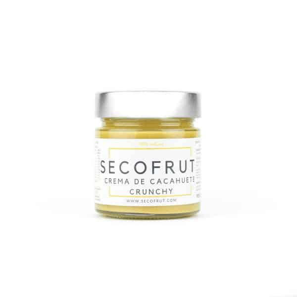 Frasco de vidrio con Crema de Cacahuete Crunchy SECOFRUT, etiquetado como '100% natural'. Se pueden ver piezas enteras y fragmentadas de cacahuete, indicando una textura crujiente. La etiqueta también muestra la URL 'WWW.SECOFRUT.COM', resaltando su compromiso con lo natural y artesanal